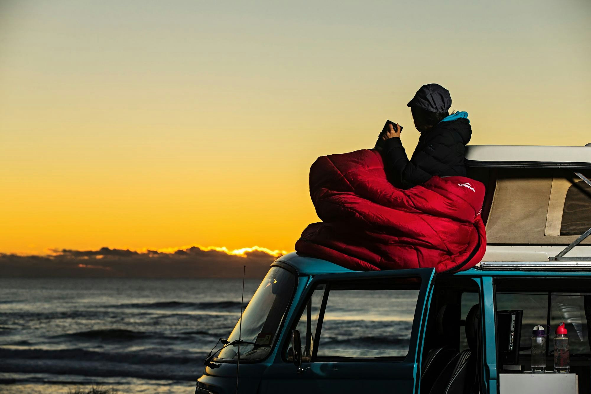 Woman sitting on top of van in sleeping bag