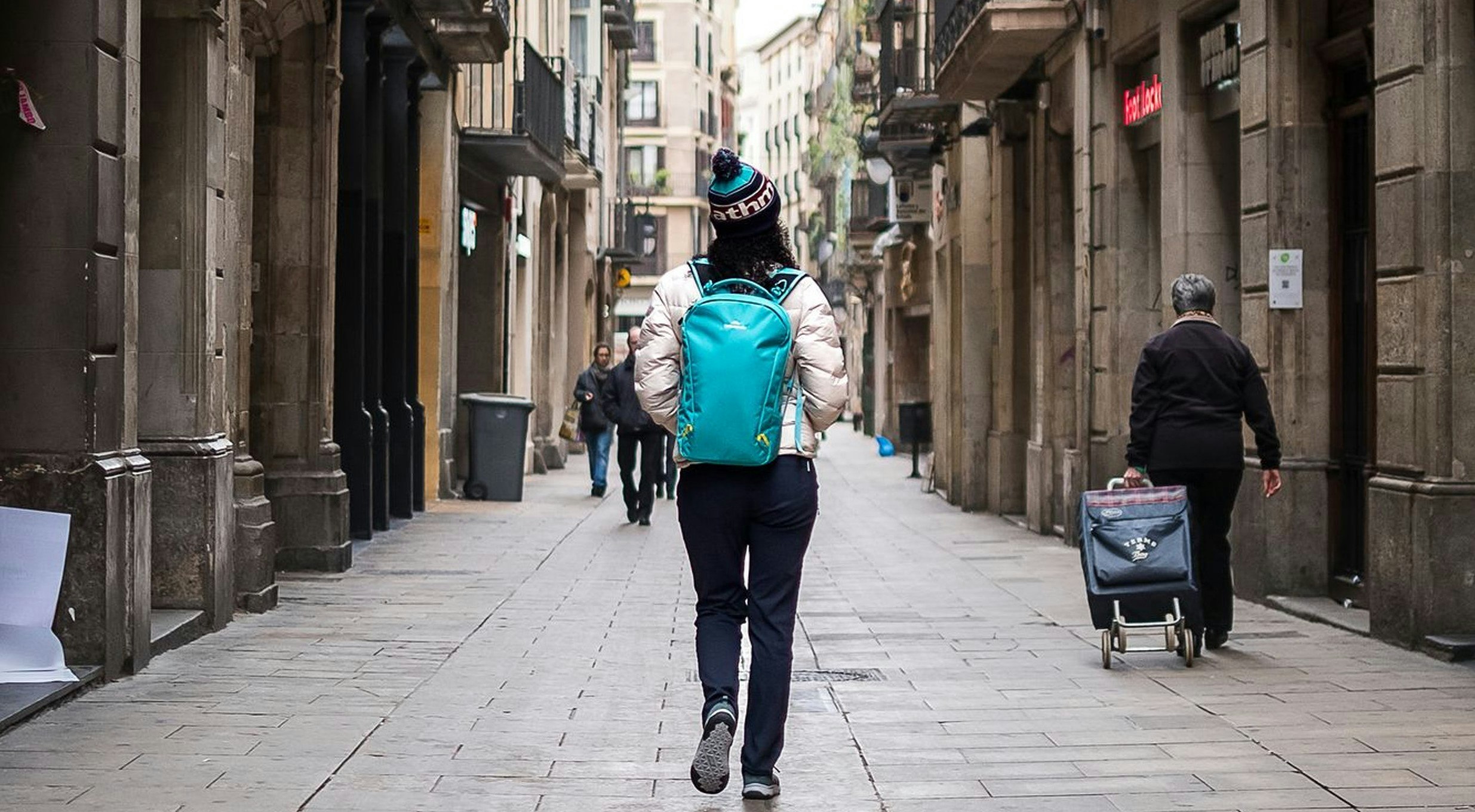 Woman wearing blue backpack walking down a European city street