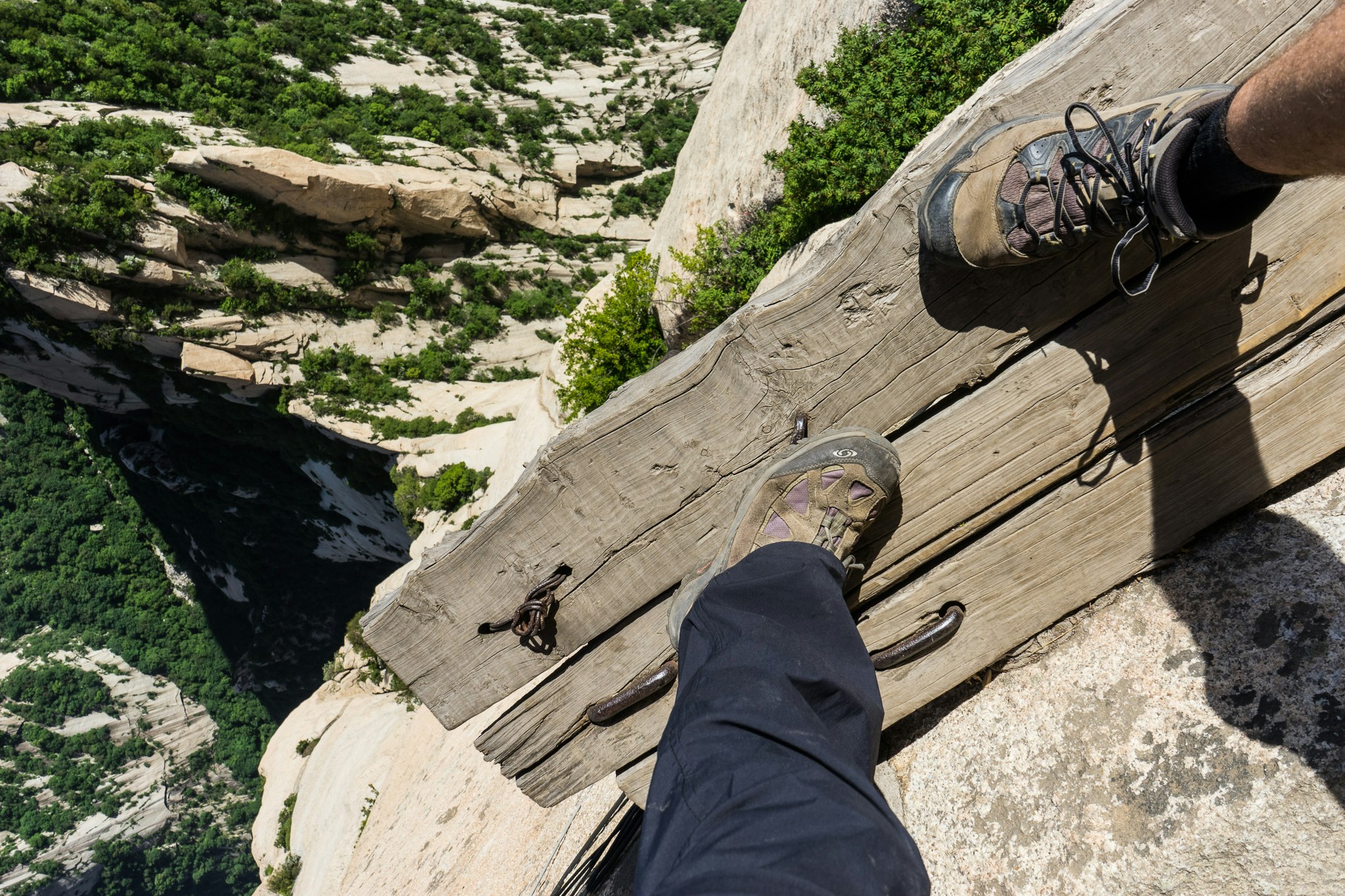 You'll need a good head of heights for Mount Huashan. Image of the camera looking over two feet and a narrow plank with a sharp descent below.