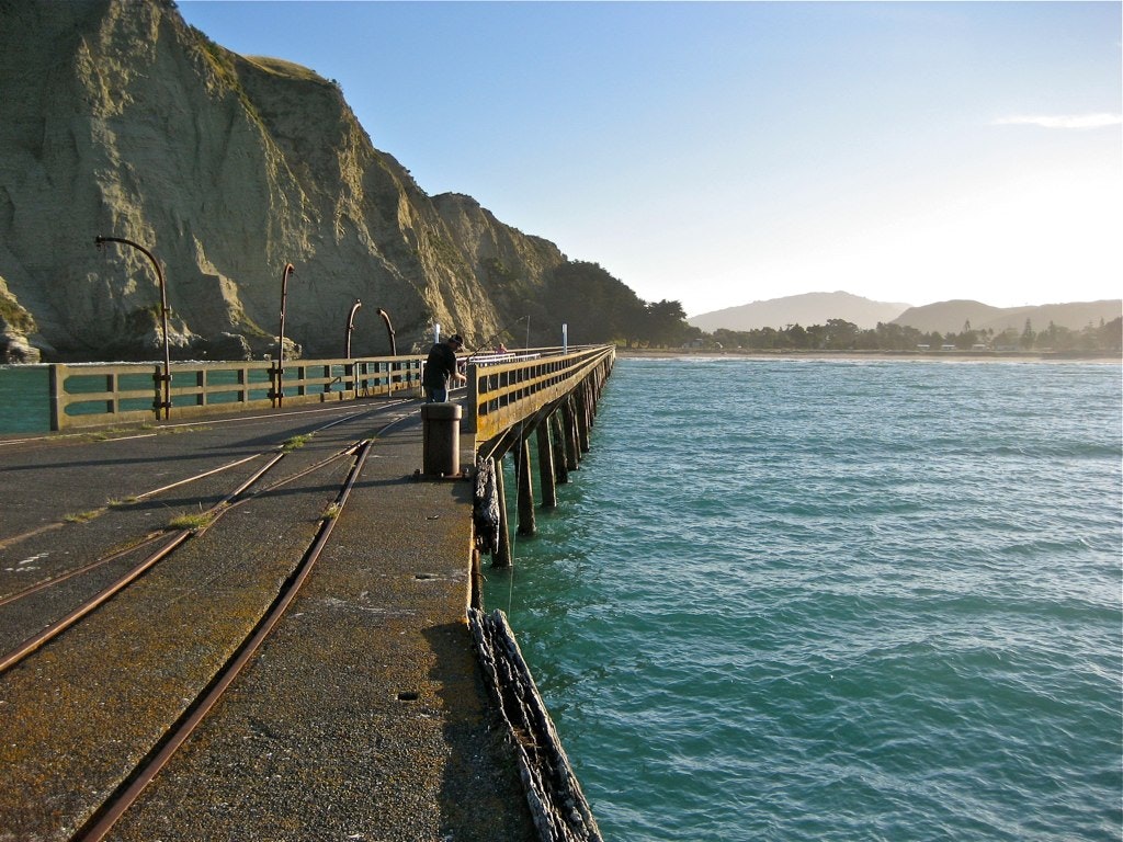 Finish up your run at the end of the pier at Tolaga Bay for a stunning view back to the coastline Man on pier at Tolaga Bay, New Zealand