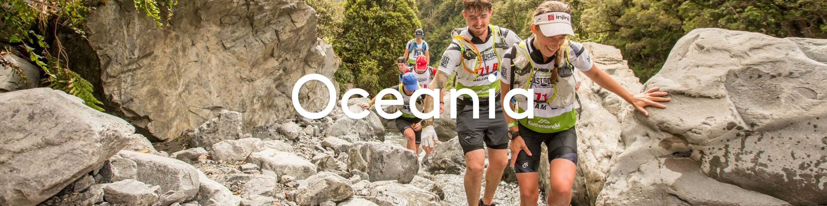 Two people running over rocks in New Zealand with 'Oceania' text overlay